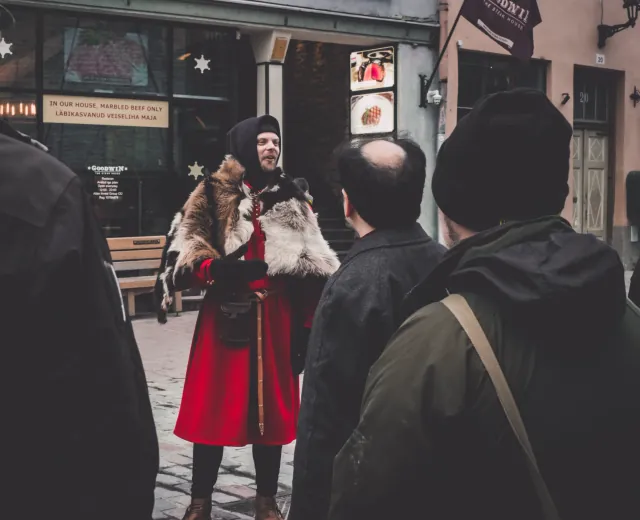 Medieval guide in a red cloak speaking to visitors on a street in Tallinn Old Town