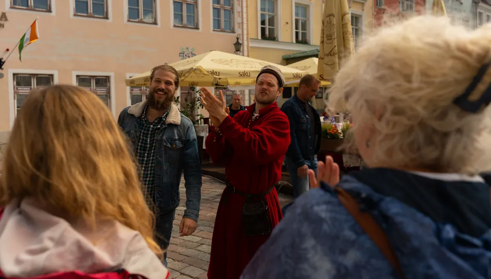 Medieval guide in a red robe speaks to a small group of visitors in Tallinn Old Town.