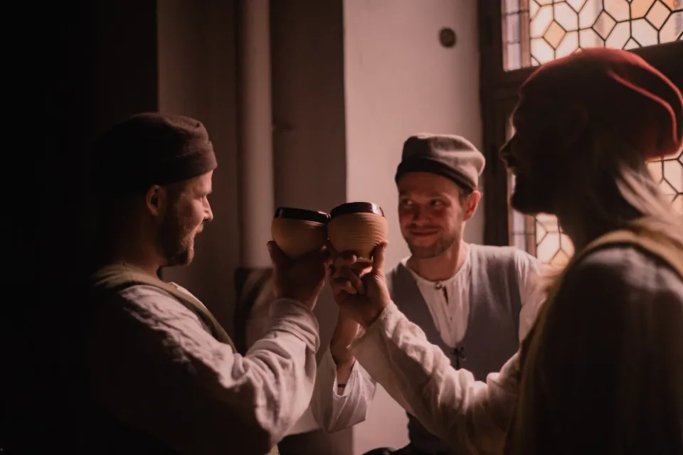 Three people in historical clothing raise a toast indoors.